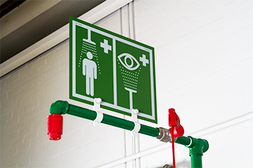 Green safety shower with red nozzle shown with emergency safety signage