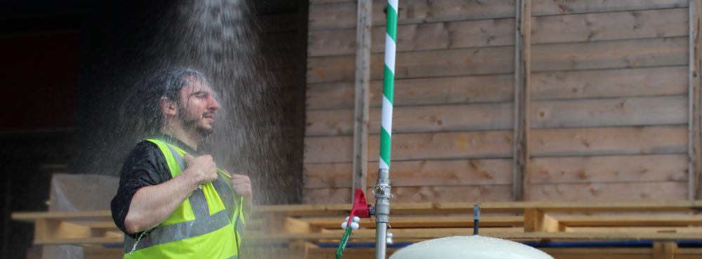 Worker in high vis standing under an activated Hughes mobile safety shower