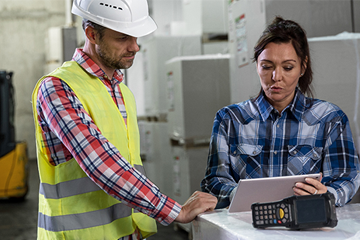 male worker in high vis and hard hat standing with female worker holding clipboard