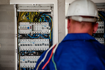 electrician in hard hat facing away from us in front of an electrical panel