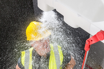 Employee standing under activated Hughes safety shower with hard hat and high-vis vest