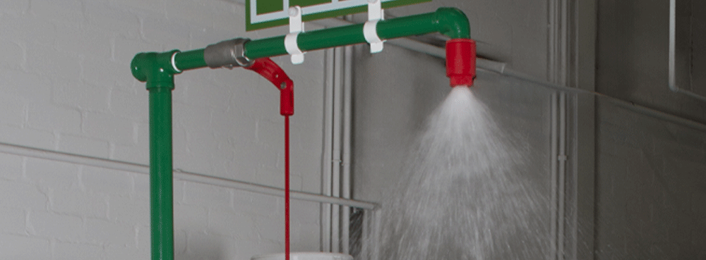 Tepid water flows from the nozzle of an indoor mains-fed laboratory safety shower unit