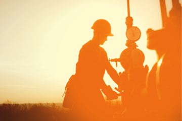 Worker in hard hat on oil field, silhouetted against an orange sky