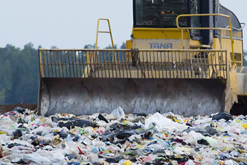 landfill with digger moving through large cluster of rubbish