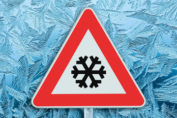 Warning road sign with snowflake symbol in front of frosty background