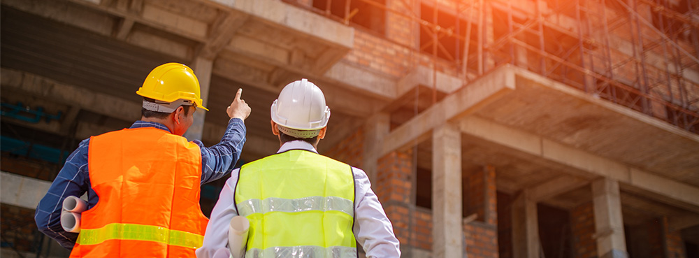 Two construction workers in high vis and hard hats observing a site