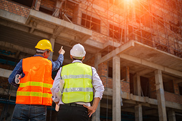 Two construction workers in high vis and hard hats observing a site