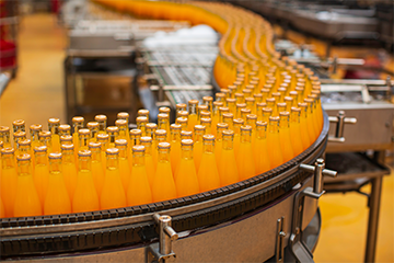 A conveyor belt full of glass bottles filled with an orange liquid 