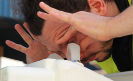 Worker holding eyes open to use Hughes eye wash