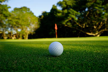 White golf ball on sunny golf course grass with hole flag in distance