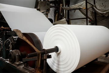 Large ream of paper being wound into roll inside production factory