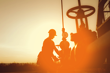Workers in hard hats controlling machinery in oilfield as the sun sets