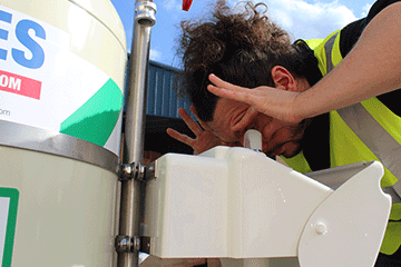 Male worker uses eye wash, leaning over it and holding his eyes open with his fingers