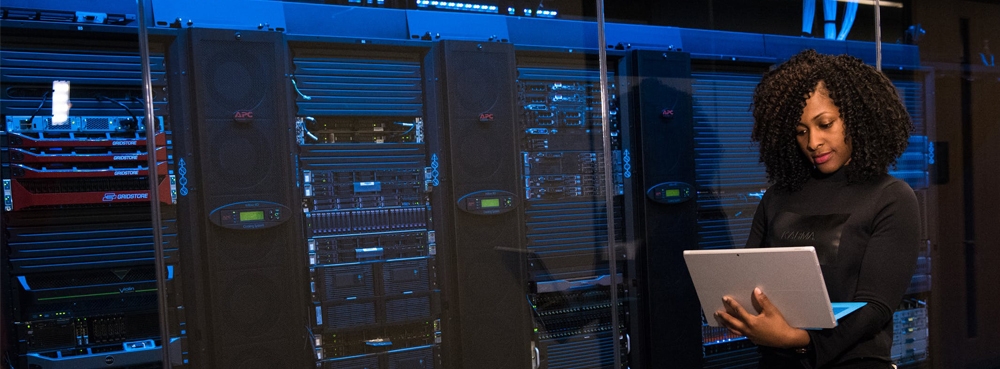 Woman on computer standing next to large computer servers