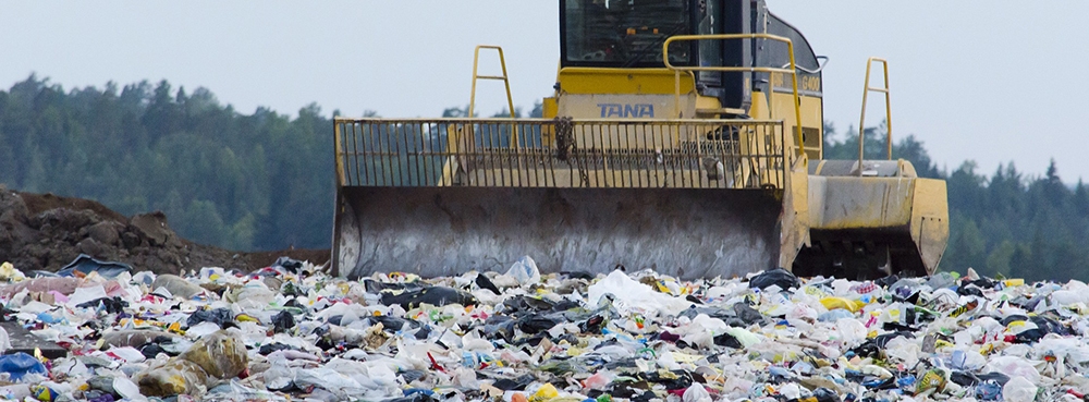 landfill with digger moving through large cluster of rubbish