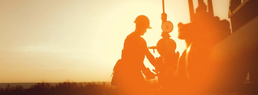 Workers in Remote Oilfield operating machinery in front of sunset