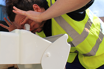 A worker in high vis uses a plumbed-in eyewash station with pull-down manifold